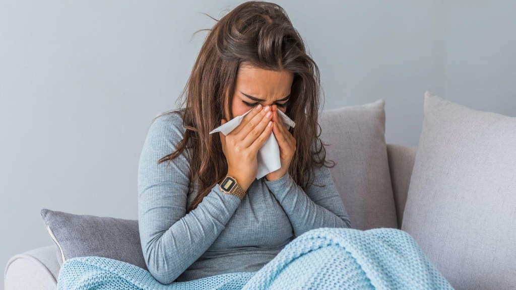 A girl sitting in couch and sneezing due to common cold
